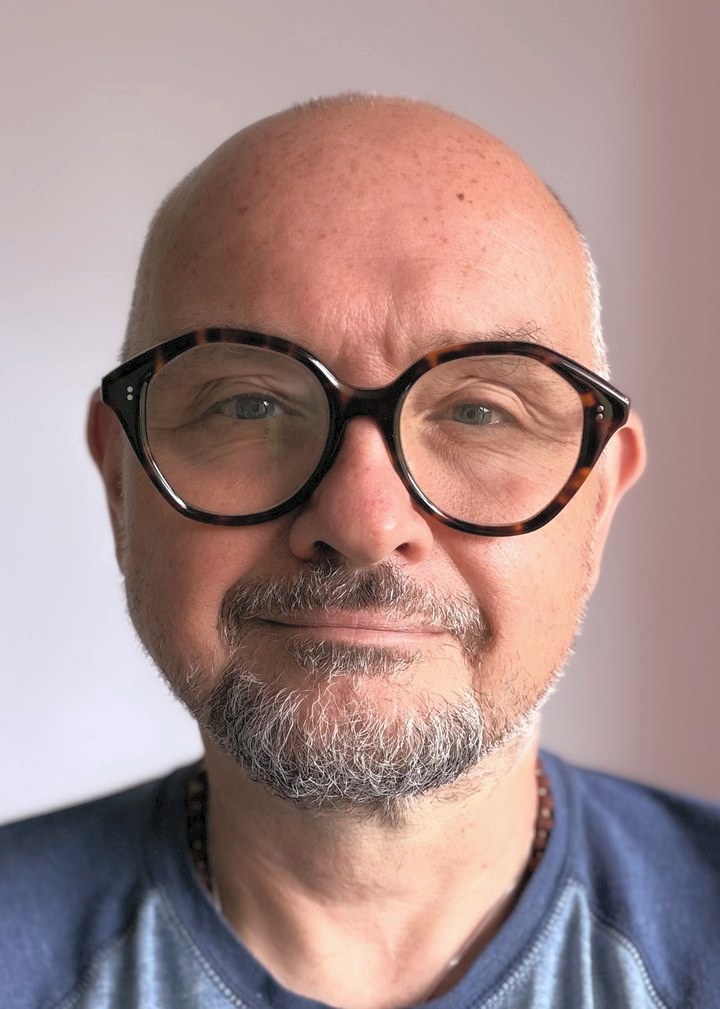 Gary Keene: a bald man with a short grey beard and dark round glasses, wearing a blue t-shirt, looking towards the camera.